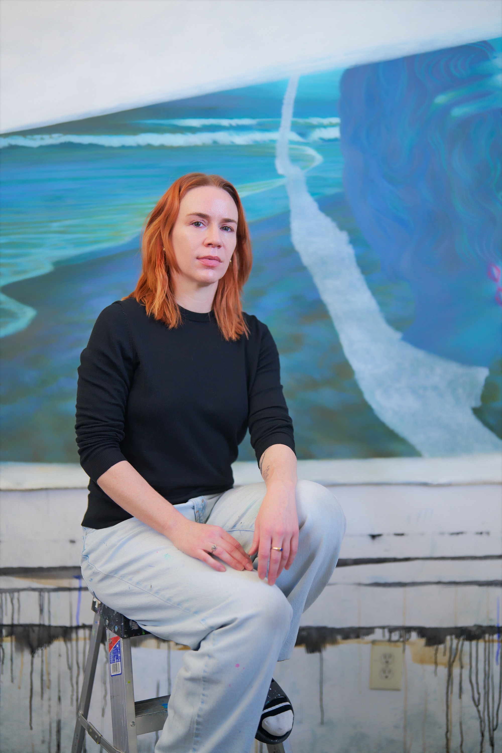 Portrait of Tess Bilhartz seated on a stepladder in her studio